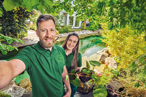 Landschaftsgärtner machen Selfie vor einem Schwimmteich und präsentieren ihre Abreit 