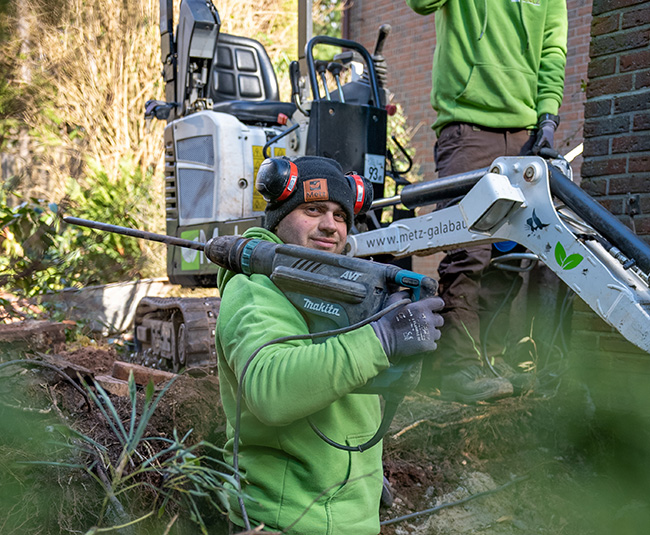 Timo Rübeck steht vor einem Kleinbagger mit einer großen Bahrmaschine auf der Schulter