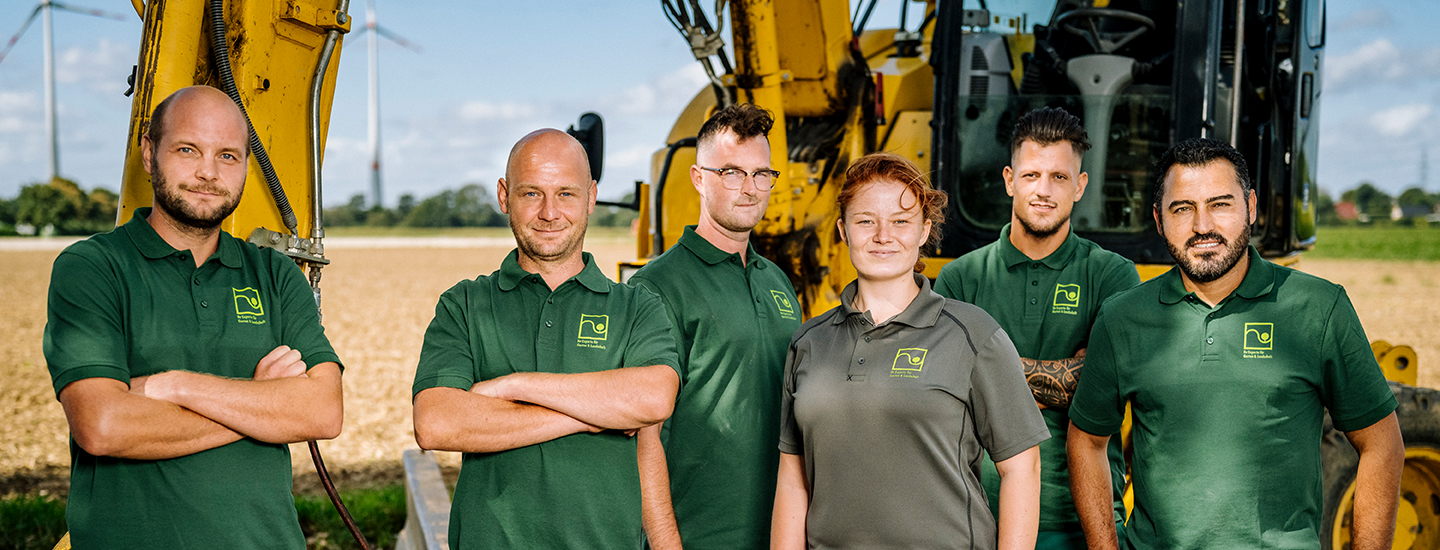 Sechs Landschaftsgärtner*innen stehen vor einem Bagger und sind zufrieden