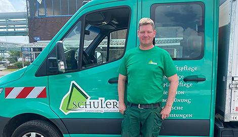 Holger steht zufrieden vor einem Wagen seines Betriebs